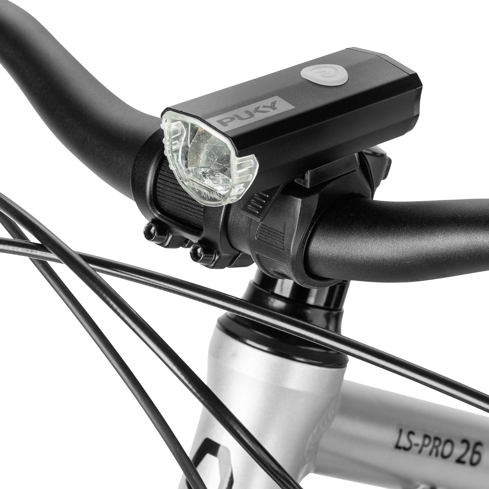 Närbild av en svart PUKY LUMI cykelstrålkastare monterad på styret på en silverfärgad cykel, med bromsvajrar och en del av ramen märkt "LS-PRO 26".