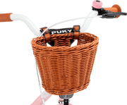 Närbild av en PUKY CHAOS KORB - M brun flätad korg fäst på ett cykelstyre med orange handtag. "PUKY"-etiketten sitter ovanför korgen och ramen är delvis rosa och vit.