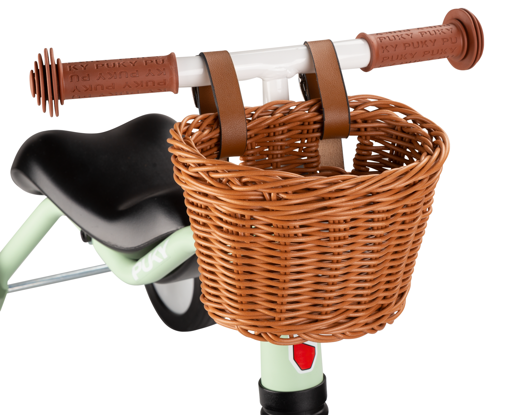 Närbild på en CHAOS KORB S flätad korg från PUKY, ljusbrun och fäst vid styret på en ljusgrön barncykel med bruna handtag och en del av en svart sadel synlig.