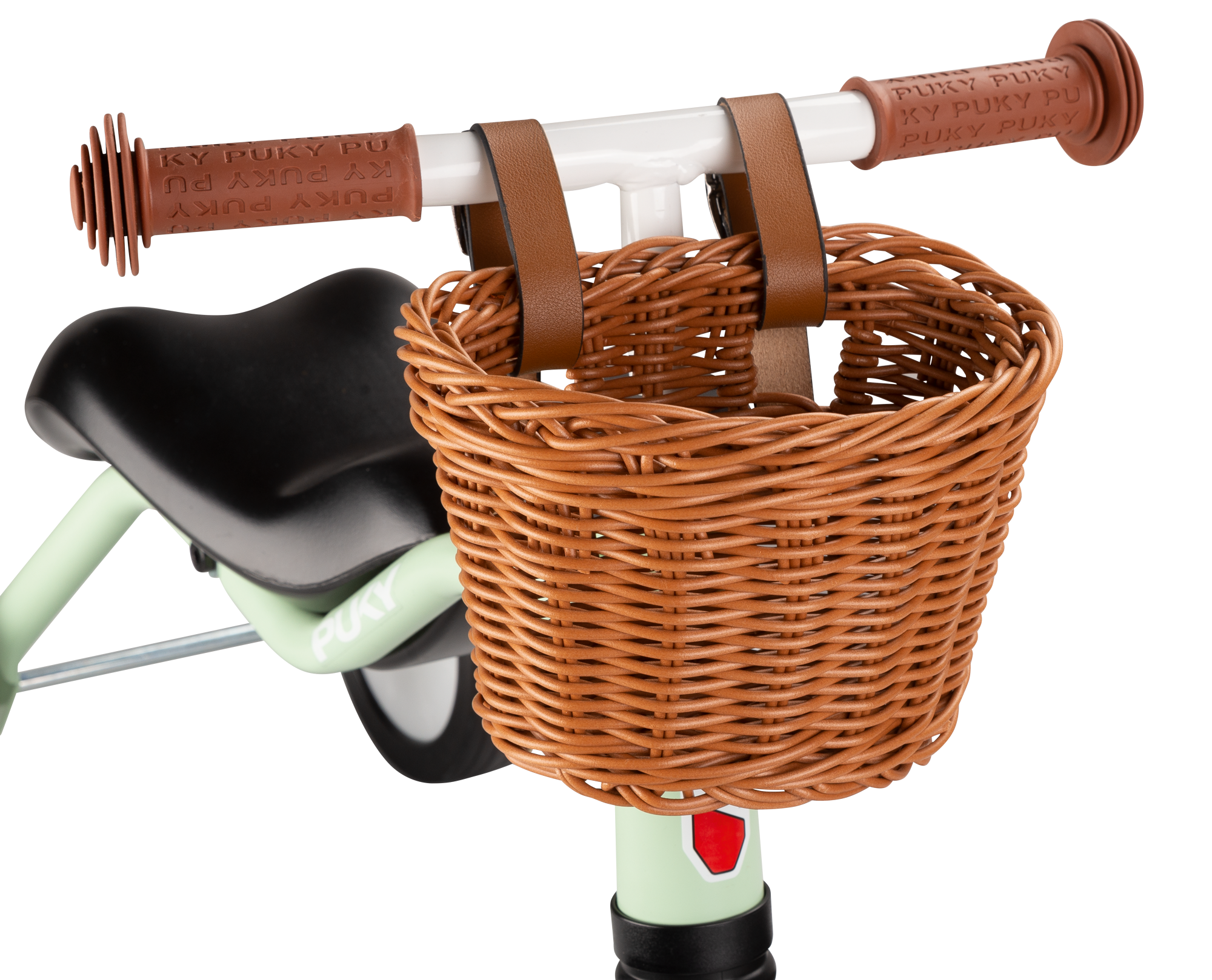 Närbild på en CHAOS KORB S flätad korg från PUKY, ljusbrun och fäst vid styret på en ljusgrön barncykel med bruna handtag och en del av en svart sadel synlig.